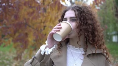 Autumn, genç bir kadın dışarıdaki kağıt bardaktan kahve ya da çay içiyor. Güz parkında kahve içen güzel bir kadın.