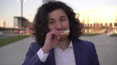 İş adamı dışarıda sandviç yiyor. Modern fast food konsepti. Başarılı genç adam atıştırıyor.