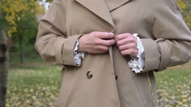 Young woman in a beige raincoat in the autumn park. The concept of fashionable autumn or spring clothes Video Clip