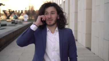 Açık havada başarılı bir iş adamı konuşuyor. Takım elbiseli genç bir adam akıllı telefondan iletişim kuruyor.