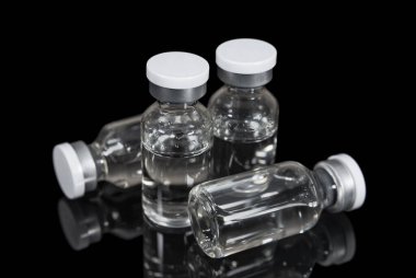 Vials with transparent vaccine on a black mirror surface. Medicines and healthcare
