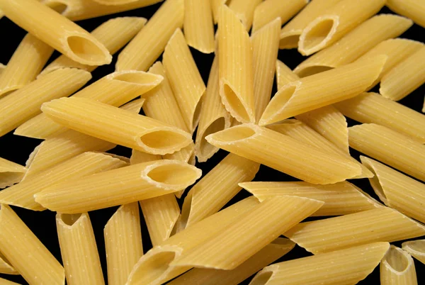 Penne rigate pasta with ridged surface on dark background. Pasta and bakery