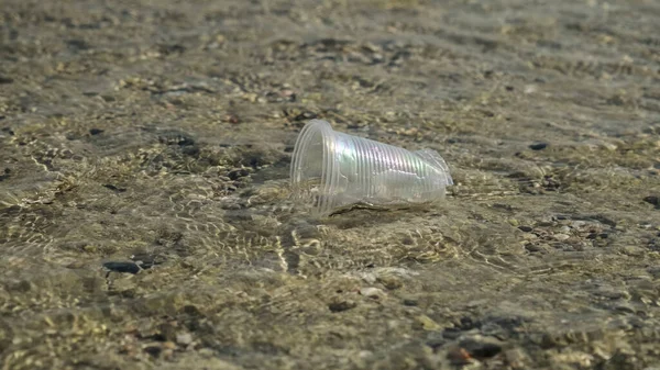 Transparent plastic cup is carried away by the wind to the sea in the coastal zone. Plastic pollution of the surf zone. Red sea, Egypt