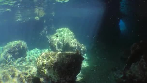 Mergulho, mergulho: a câmera se move para a entrada escura da gruta acima das pedras iluminadas por raios de sol. — Vídeo de Stock