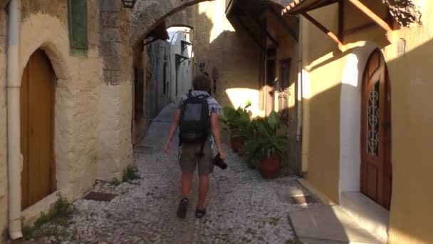 Ένας άντρας με κάμερα περπατάει κατά μήκος του δρόμου της Παλιάς Πόλης. Ρόδος, Ελλάδα. — Αρχείο Βίντεο