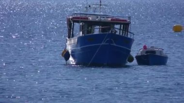 Deniz yüzeyinden yansıyan güneş ışınları demirlemiş iki zevk teknesinin gövdesinde oynar..