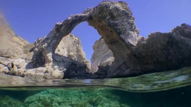 Camera attraversa la superficie dell'acqua, prima mostra la roccia costiera sotto forma di un arco, poi un fondo roccioso, diviso. — Video Stock