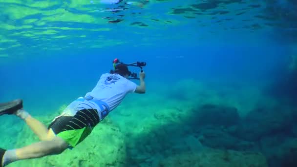 Фридайвер с камерой уплывает вдоль скалистой прибрежной скалы. — стоковое видео