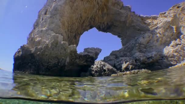 Caméra traverse la surface de l'eau, en même temps montre un fond rocheux et rocher côtier sous la forme d'un arc, divisé . — Video