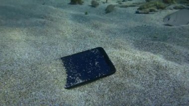 Kumlu zeminde, arka planda, su altında kaybolmuş akıllı telefon..