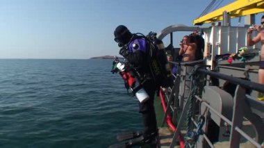Teknik dalgıç uzak bir adanın arka planında gemiden suya atlar..