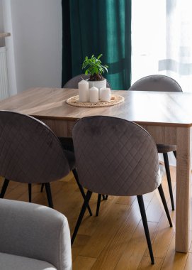 Gri kanepesi, yeşil perdesi, gri sandalyeleri ve bitkisi olan, ahşap mutfak masasında beyaz mumları olan şık bir oturma odası. Modern ev dekorasyonu