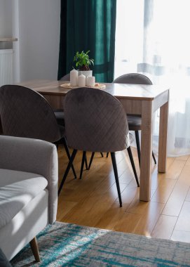 Gri kanepesi, yeşil perdesi, gri sandalyeleri ve bitkisi olan, ahşap mutfak masasında beyaz mumları olan şık bir oturma odası. Modern ev dekorasyonu