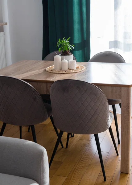 Gri kanepesi, yeşil perdesi, gri sandalyeleri ve bitkisi olan, ahşap mutfak masasında beyaz mumları olan şık bir oturma odası. Modern ev dekorasyonu
