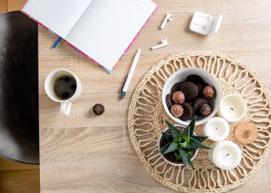 Yarın sabah planlama var. Bir fincan kahve, bir kase çikolata ve kurabiye, kablosuz kulaklık, defter, kalem, mum ve masada ev yapımı çiçek. Planlama ve evde eğitim kavramı.