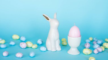 Paskalya kartı. Paskalya porselen tavşanı, boyalı yumurtalar ve mavi arka planda beyaz bir saksıda sarı bir çiçek. Sarı-mavi konsept.