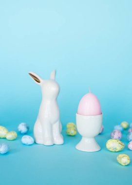 Paskalya kartı. Paskalya porselen tavşanı, boyalı yumurtalar ve mavi arka planda beyaz bir saksıda sarı bir çiçek. Sarı-mavi konsept.