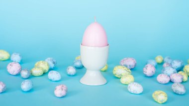 Paskalya kartı. Paskalya porselen tavşanı, boyalı yumurtalar ve mavi arka planda beyaz bir saksıda sarı bir çiçek. Sarı-mavi konsept.