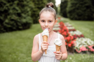 Küçük kız parkta dondurma yiyor. Çocuk yazın dondurmanın tadını çıkarıyor. Kızın elinde bir dondurma külahı var..