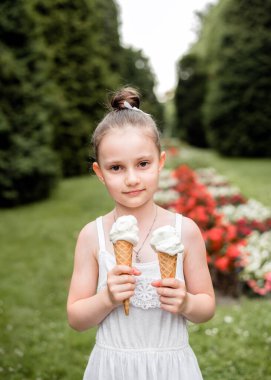 Küçük kız parkta dondurma yiyor. Çocuk yazın dondurmanın tadını çıkarıyor. Kızın elinde bir dondurma külahı var..
