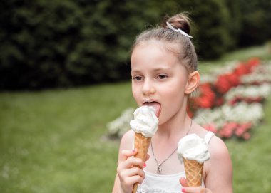 Küçük kız parkta dondurma yiyor. Çocuk yazın dondurmanın tadını çıkarıyor. Kızın elinde bir dondurma külahı var..