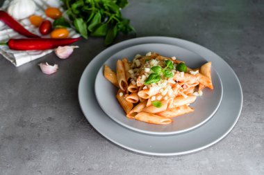 Gri arka planda fesleğen ve peynirli makarna. Tipik İtalyan makarna arrabbiata soslu makarna..  