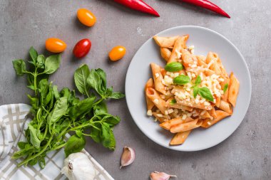 Gri arka planda fesleğen ve peynirli makarna. Tipik İtalyan makarna arrabbiata soslu makarna..  