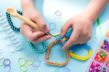 Bir kız lastik bantlardan gökkuşağı bileziği yapıyor. Lastik bantlarla dekoratif bilezik yapmaya yakın. Loom bilezikleri