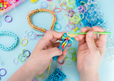 Bir kız lastik bantlardan gökkuşağı bileziği yapıyor. Lastik bantlarla dekoratif bilezik yapmaya yakın. Loom bilezikleri