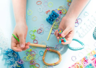 Bir kız lastik bantlardan gökkuşağı bileziği yapıyor. Lastik bantlarla dekoratif bilezik yapmaya yakın. Loom bilezikleri