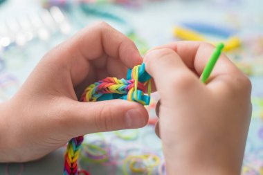 Bir kız lastik bantlardan gökkuşağı bileziği yapıyor. Lastik bantlarla dekoratif bilezik yapmaya yakın. Loom bilezikleri
