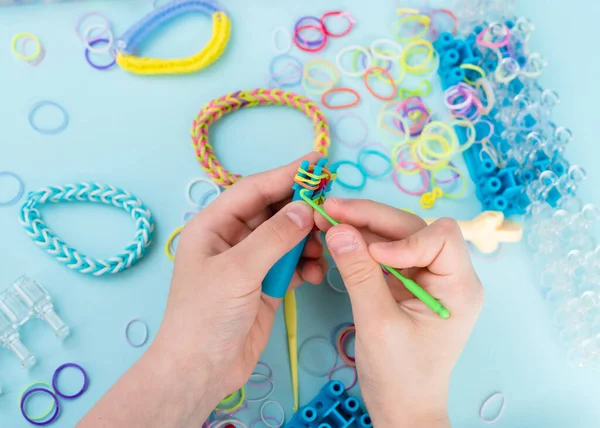 A girl makes a rainbow bracelet from rubber bands crochet. Closeup of making decorative bracelet with elastic bands. Loom bracelets