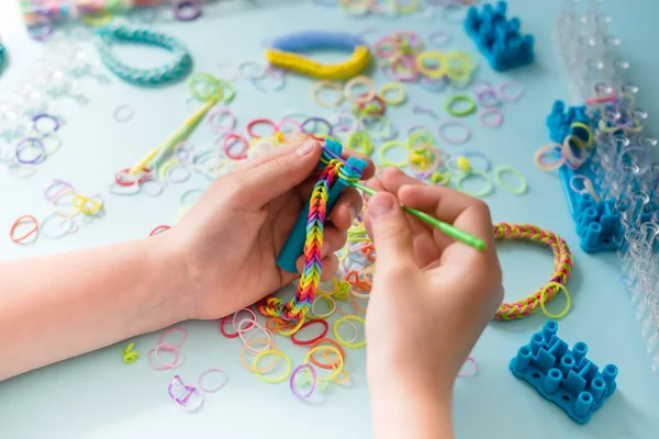A girl makes a rainbow bracelet from rubber bands crochet. Closeup of making decorative bracelet with elastic bands. Loom bracelets