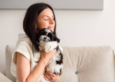 Genç ve güzel bir kadın bir shih tzu köpeğine sarılıyor ve nazikçe okşuyor. Hayvanlar ve insan dostluğu