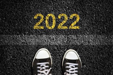2022 'de asfalt yol yüzeyinde, ve şerit işaretinin önünde spor ayakkabıları. Üst Manzara. Yeni yıl konsepti, yeni planlar ve fikirler. İş, yaşam tarzı.
