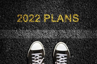 2022 yılı. Planlar, asfalt yol yüzeyinde ve şerit işaretinin önünde spor ayakkabılar. Üst Manzara. Yeni yıl konsepti, yeni planlar ve fikirler. İş, yaşam tarzı.