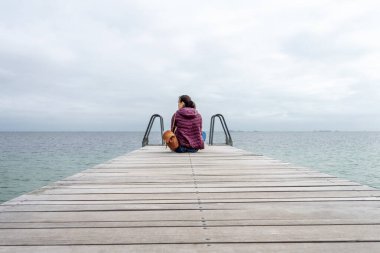 Sırt çantalı genç bir kız, denize bakıyor, ahşap bir iskelede oturuyor. Özgürlük için. Mahremiyet. Adaylık