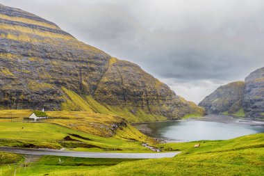 Deniz koyunda, güzel dağların ve dramatik bulutların ardında. Faroe adaları. Danimarka. Avrupa. Manzaralar.