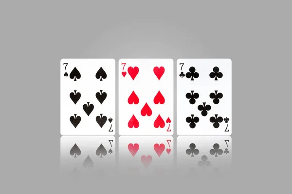 Three sevens. Playing cards on a gray background. Reflection. Gambling. Background.