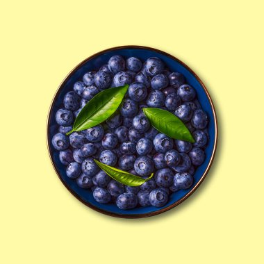 Blueberries with green leaves in a bowl, isolated on a yellow background. Healthy food. Diet. Top view. Berries.