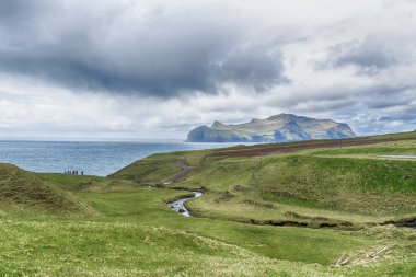 A group of people on the seashore. Beautiful island, beautiful mountains, and beautiful clouds in the blue sky. Faroe Islands. Denmark. Europe. Landscapes. Nature.