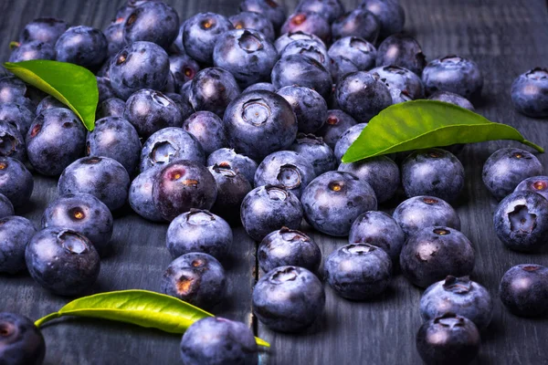 Blueberries with green leaves, on a dark blue wooden background. Close-Up. Healthy food. Diet. Top view. Berries.