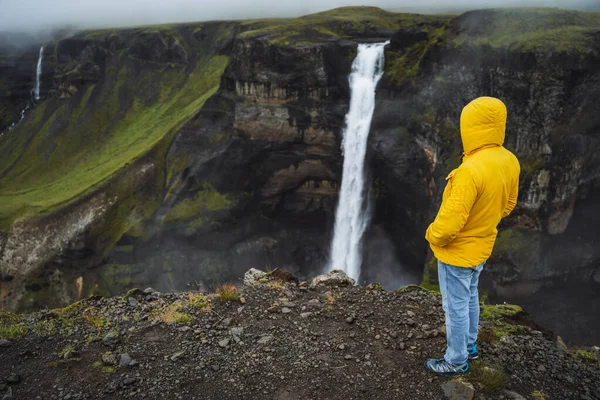 Ένας άντρας με κίτρινο μπουφάν που απολαμβάνει τον καταρράκτη Χαϊφός σε βροχερό συννεφιασμένο καιρό. Highlands της Ισλανδίας — Φωτογραφία Αρχείου