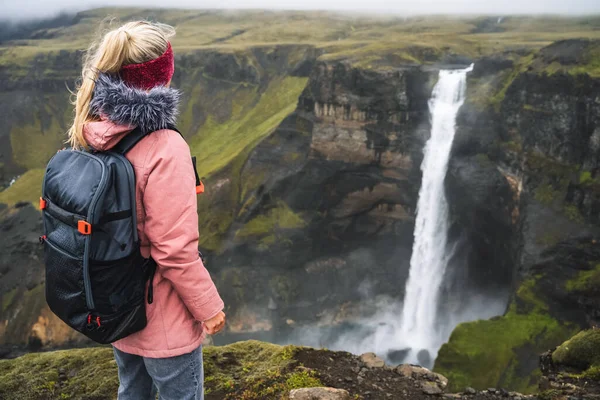 Mulher com mochila e casaco lilás desfrutando da cachoeira Haifoss da Islândia Highlands em Thjorsardalur Valley — Fotografia de Stock