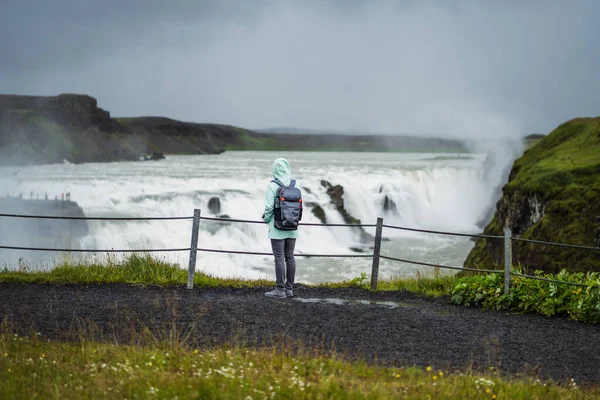 Mulher com mochila e casaco verde visitar Gullfoss poderosa cachoeira famosa na Islândia. Atração turística que seguem a rota Golden Circle da Islândia — Fotografia de Stock
