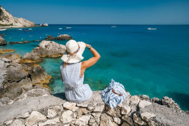 Şapkalı bir turist kadın, Yunanistan 'ın Lefkas Adası' ndaki Agios Nikitas köyünde iyon denizinin keyfini çıkarıyor.