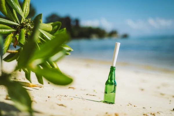 Bottle with message on white paradise sandy beach with blurred jungle in background conceptual.