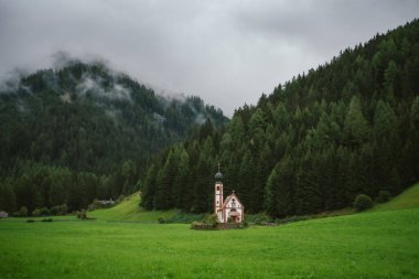 Bulutlu bir günde Ranui 'deki St. Johann Kilisesi, Dolomite Alpleri, Vilnoss Vadisi, Güney Tyrol, İtalya. Sis, çam ağacı ormanında gevşiyor..