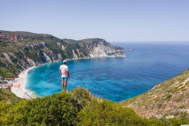 Bir kayanın tepesinde duran adam heyecan verici bir özgürlük duygusuyla Petani Sahili 'ne bakıyor. Kefalonia İyonya Adası, Yunanistan.
