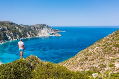Bir kayanın tepesinde duran adam heyecan verici bir özgürlük duygusuyla Petani Sahili 'ne bakıyor. Kefalonia İyonya Adası, Yunanistan.